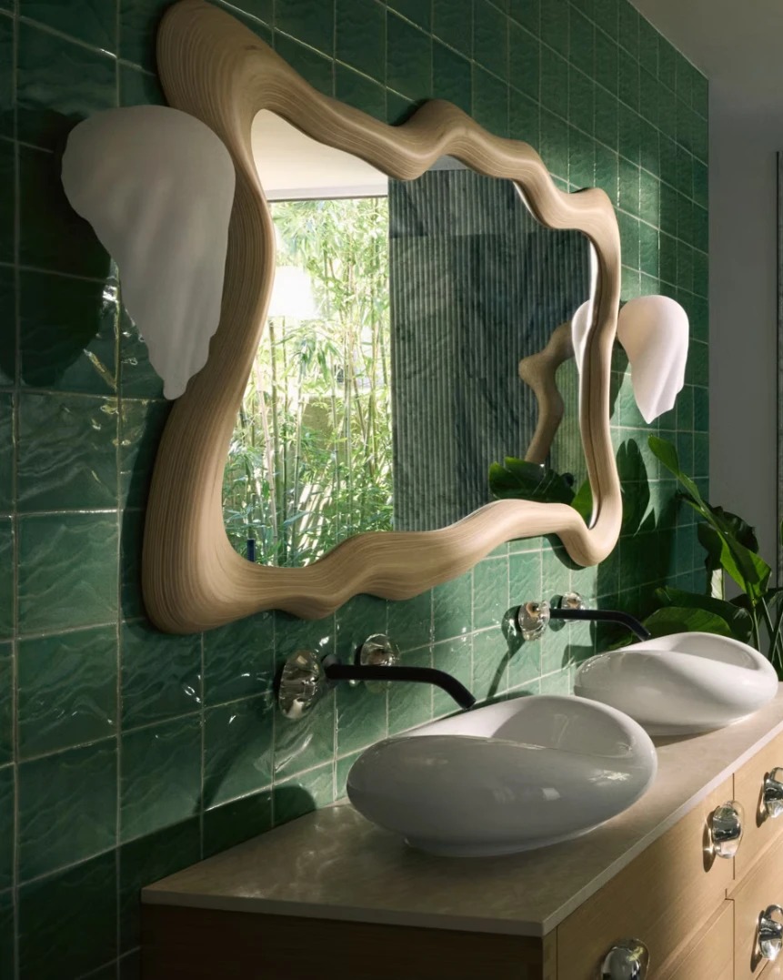 Sculptural carved mirrors and double vanity against deep green tile